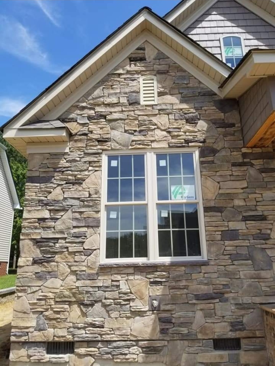 Modern stone-clad house with large white-framed windows and peaked roof