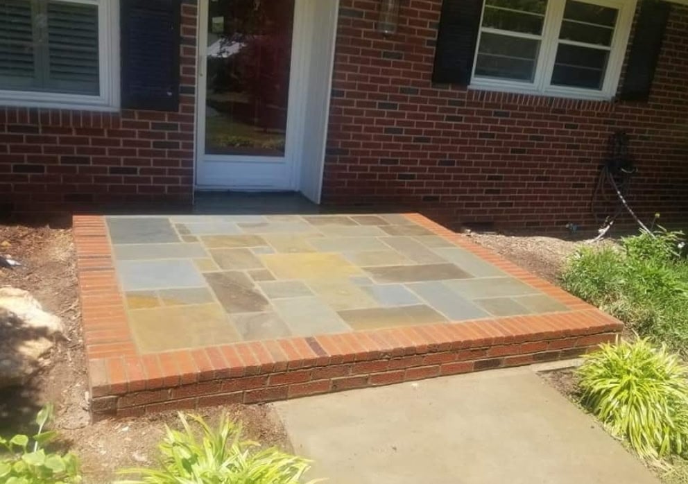Newly installed patio with mixed-color stone tiles and red brick border