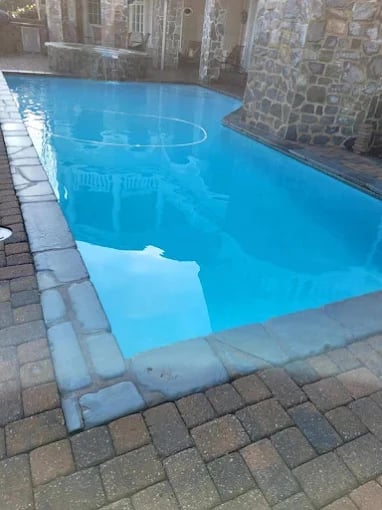 Rectangular swimming pool with bright blue water and stone patio surrounded by historic stone buildings
