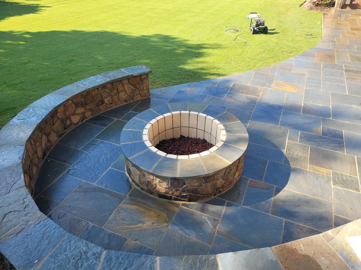Circular stone fire pit with metal ring on paved patio overlooking green lawn with curved seating wall