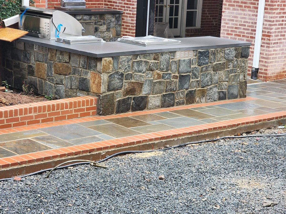 Stone and brick patio with seating wall beside brick building and gravel driveway