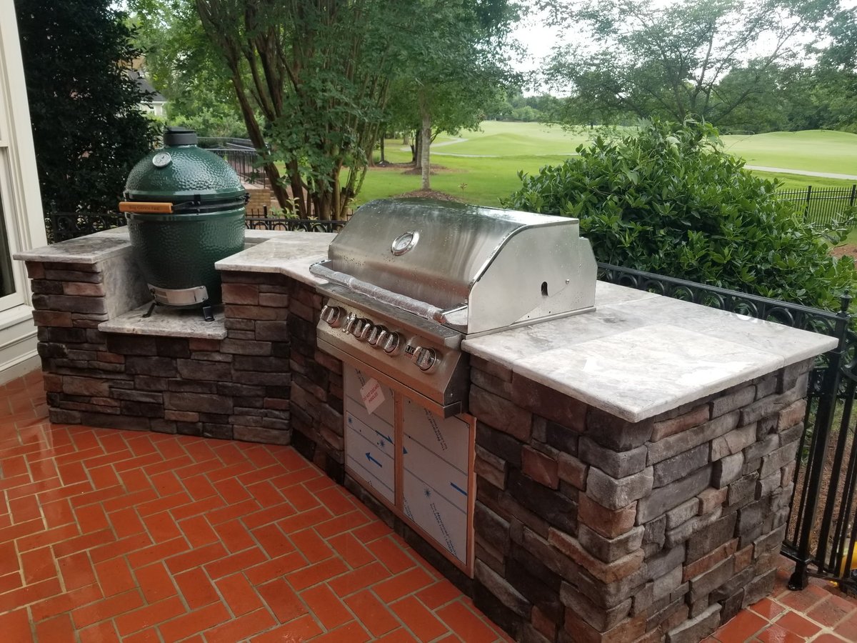 Outdoor brick kitchen with gas grill, smoker, and work counter overlooking green yard